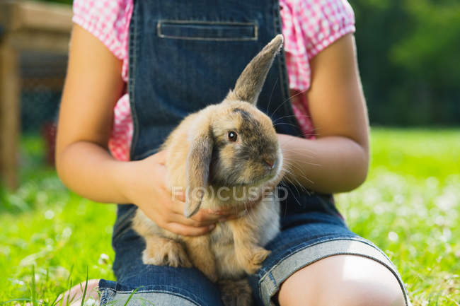 Immagine ritagliata di bambino che tiene il coniglio in cortile — Foto stock