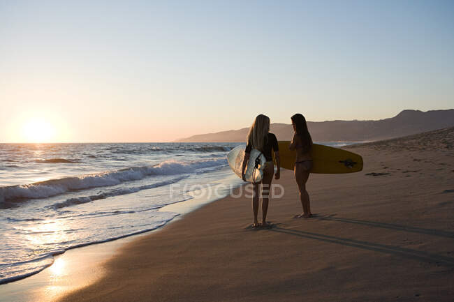 Female surfers by the sea at sunset — Stock Photo