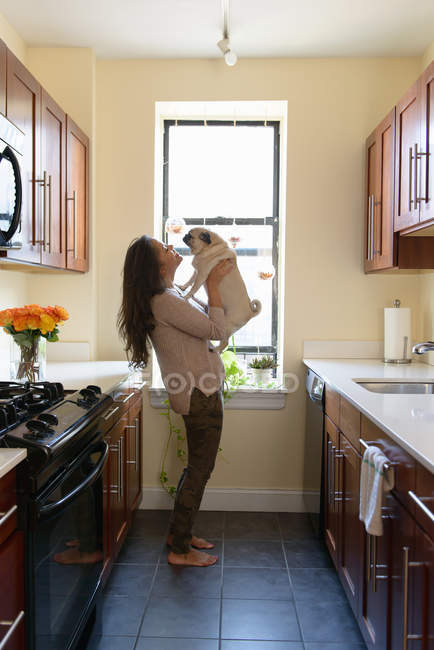 Молода жінка стоїть на кухні тримає собаку — стокове фото