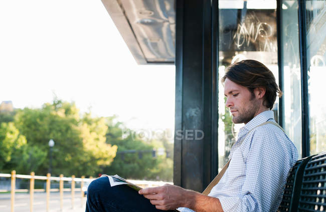 Человек ждет на вокзале и читает газету — стоковое фото