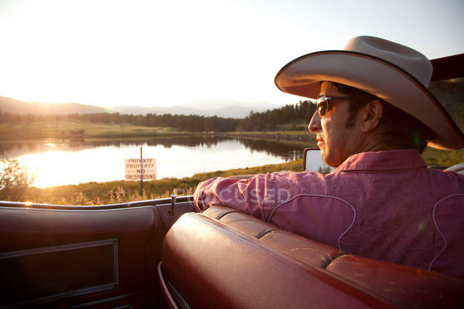 Uomo in cappello da cowboy, guardando il lago dalla sua auto — Foto stock