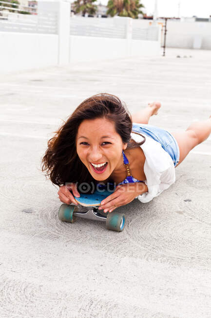 Жінка на парковці лежить на скейтборді — стокове фото