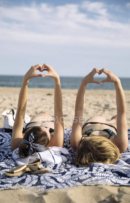 Women lying on beach blanket, showing heart-shaped gesture, Amagansett, New York, USA — Stock Photo
