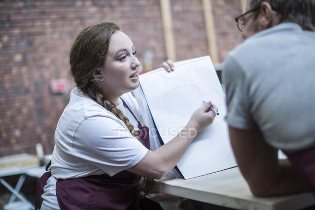 Cape Town, South Africa, young woman sketching out plans on notebook to instructor in ceramic workshop — Stock Photo