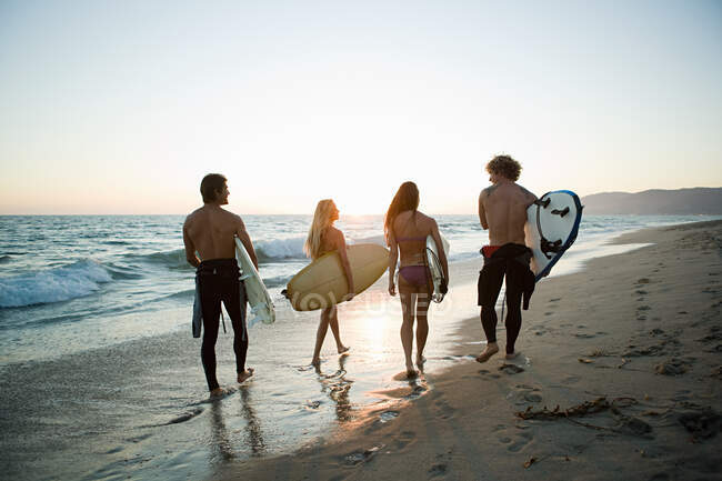 Rear view of surfers on the beach at sunset — Stock Photo