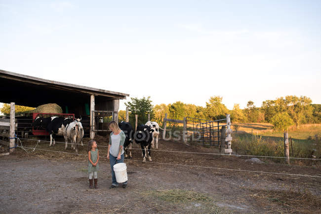 Madre e hija de pie juntas en la granja, sosteniendo la alimentación animal - foto de stock