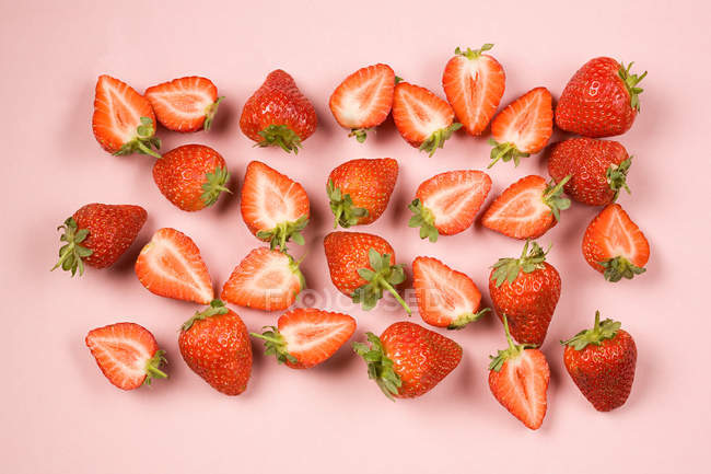 Ganze und halbierte Erdbeeren auf rosa Hintergrund — Stockfoto