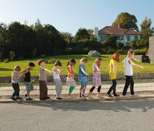 Ragazzi e ragazze in equilibrio sul marciapiede, vista laterale — Foto stock