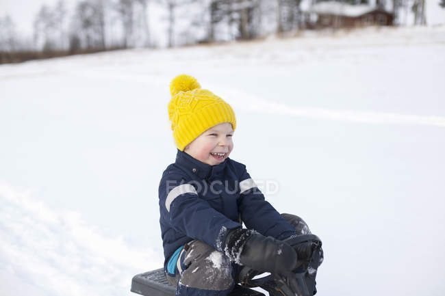 Kleiner Junge sitzt auf Schlitten, in verschneiter Landschaft — Stockfoto