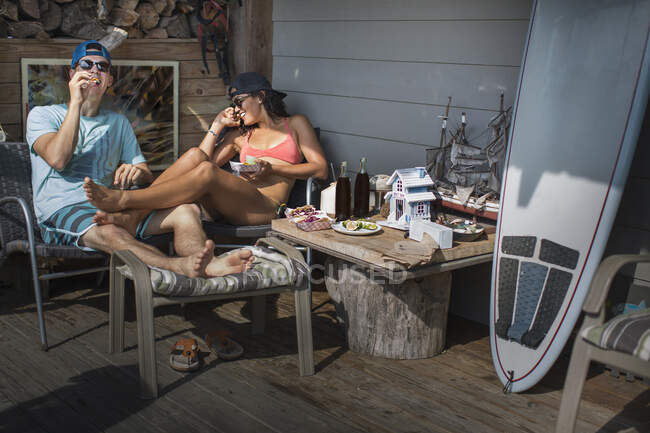 Couple on porch eating snacks, Rockaway Beach, New York, Estados Unidos. - foto de stock