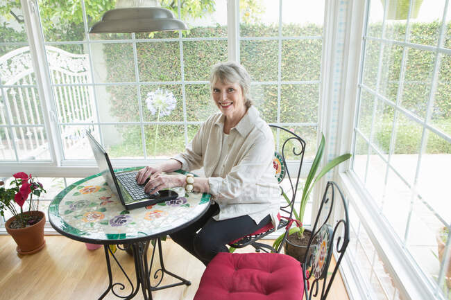 Senior woman using latpop in conservatory, portrait — Stock Photo