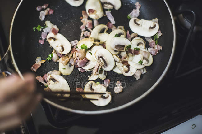 Jovem mulher mexendo cogumelos fatiados na frigideira, vista aérea — Fotografia de Stock