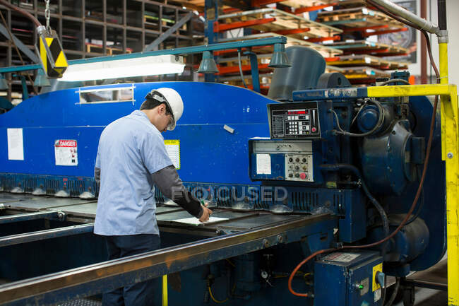Trabajador que utiliza maquinaria en planta de metal - foto de stock