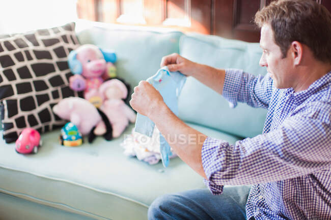 Uomo pieghevole vestiti bambino sul divano — Foto stock