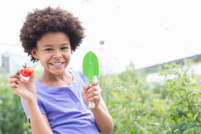 Girl holding tomato and trowel — Stock Photo