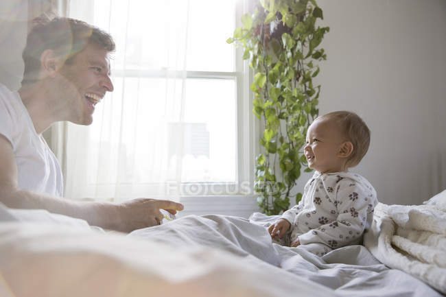 Отец и маленький сын, сидя в постели, играют — стоковое фото