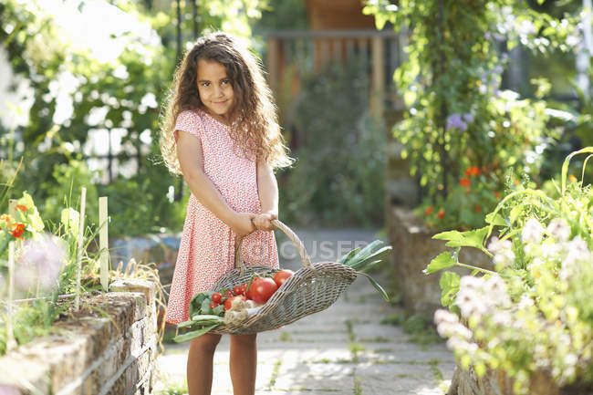 Retrato de niña bonita sosteniendo cesta de verduras frescas en el jardín - foto de stock
