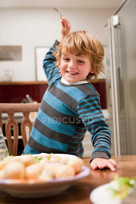 Giovane ragazzo con forchetta sollevato per pugnalare la patata — Foto stock