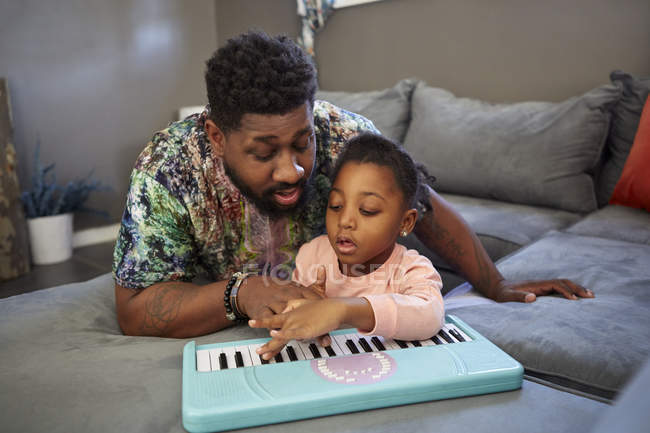 Mädchen liegt mit Vater auf Sofa und spielt Spielzeugtastatur — Stockfoto