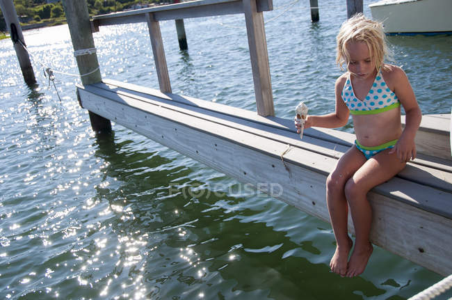 Girl sitting on pier and holding ice cream — Stock Photo