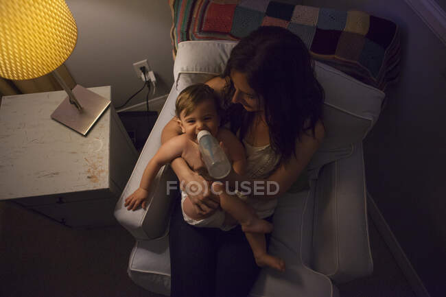 High angle view of mother in armchair feeding baby boy from baby bottle — Stock Photo