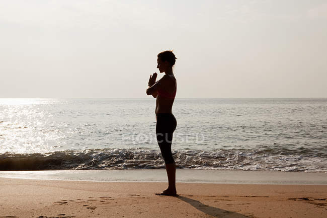 Silhouette of woman by sea in prayer pose — Stock Photo