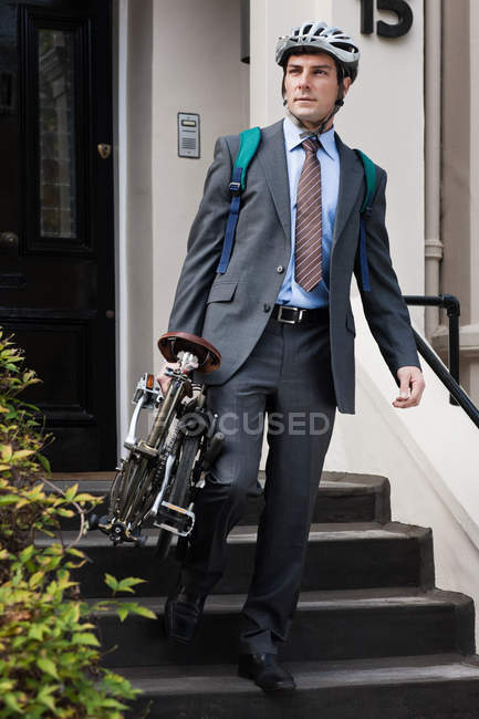 Mid adult businessman carrying folding bicycle down steps — Stock Photo