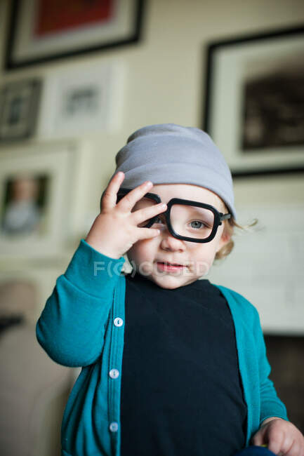 Portrait of male toddler in knit hat trying on eye glasses — Stock Photo