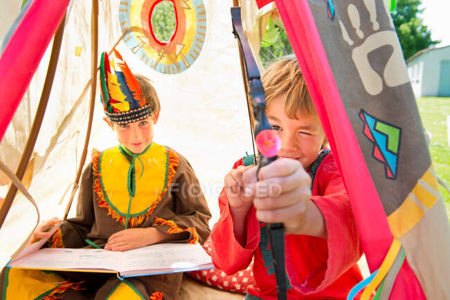 Irmãos vestidos com trajes nativos americanos brincando em teepee, retrato — Fotografia de Stock