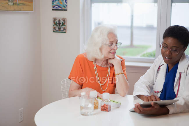 Mulher sênior e médico usando tablet computador à mesa — Fotografia de Stock