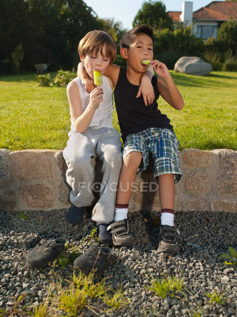 Jungen sitzen an der Wand und genießen Eisloliies, Portrait — Stockfoto