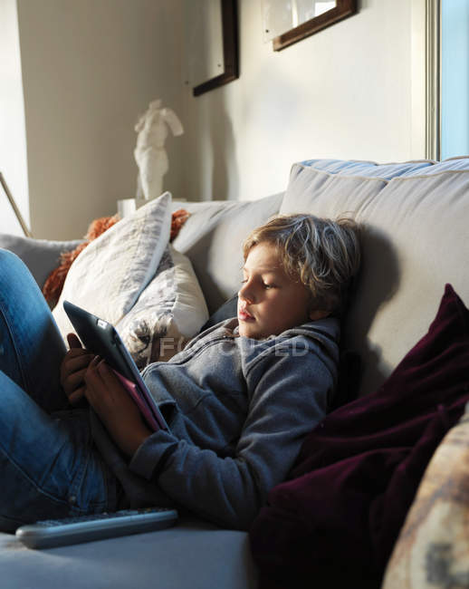 Підлітковий хлопчик розслабляється на дивані і використовує цифровий планшет — стокове фото