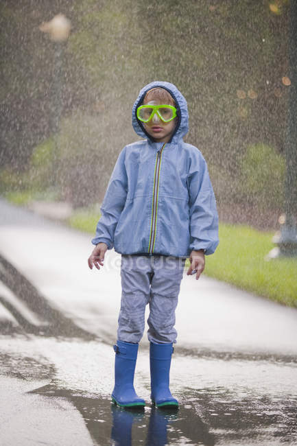 Portrait of boy wearing scuba goggles and rubber boots standing in street puddle — Stock Photo