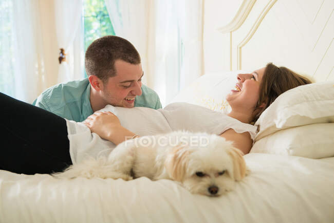 Pregnant woman and partner lying on bed with dog — Stock Photo
