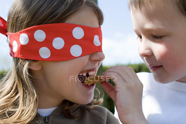 Хлопчик годує печиво дівчині в зав'язаних очима — стокове фото