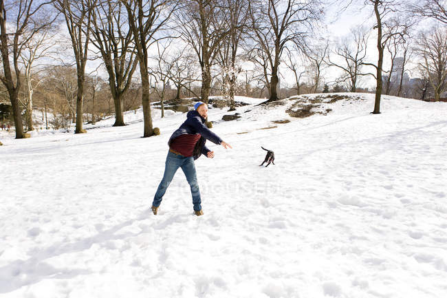 Jeune homme jouant avec un chien à Central Park enneigé, New York, USA — Photo de stock