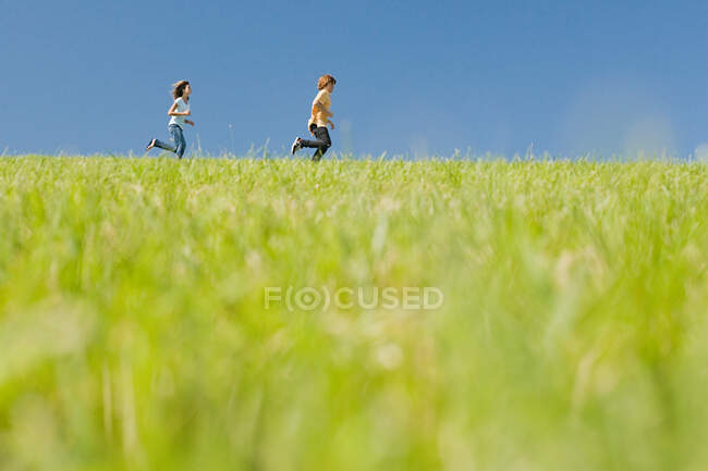 Chico y chica corriendo en el campo - foto de stock