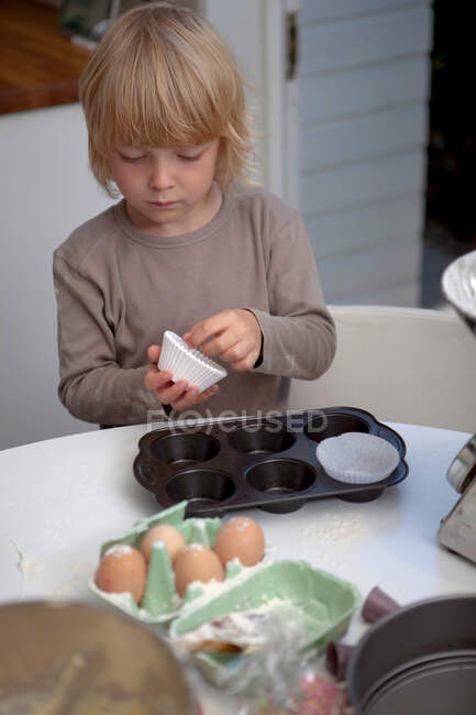 Мальчик кладет кейсы в лоток для кексов — стоковое фото