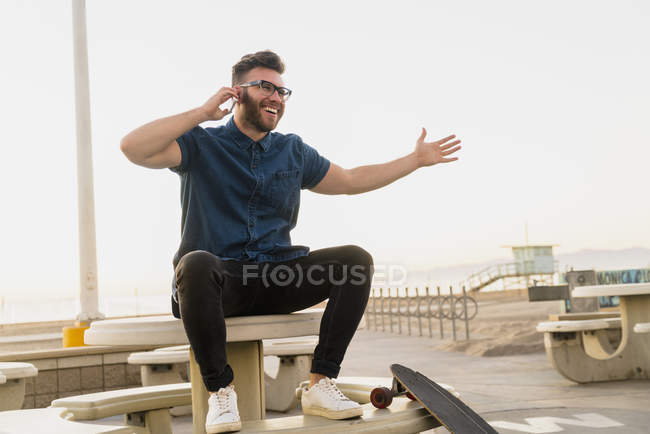 Молодий чоловік сидить на відкритому повітрі, використовуючи смартфон, сміючись — стокове фото
