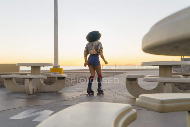 Mid adult woman on rollerskates, near beach, rear view — Stock Photo