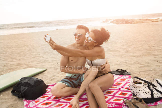 Pareja joven tomando selfie de teléfonos inteligentes en Rockaway Beach, Estado de Nueva York, Estados Unidos - foto de stock