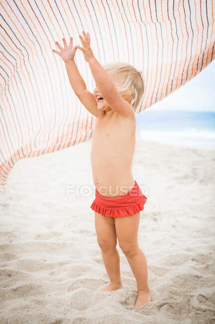 Тоддлер поднимает руки, чтобы поймать полосатое полотенце — стоковое фото