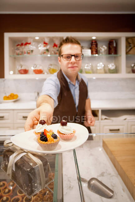 Kassiererin hält Teller mit Torten in Bäckerei — Stockfoto
