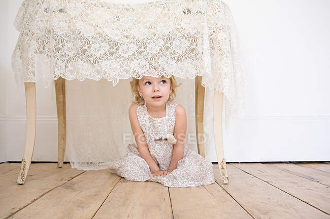 Chica escondida debajo de una mesa - foto de stock