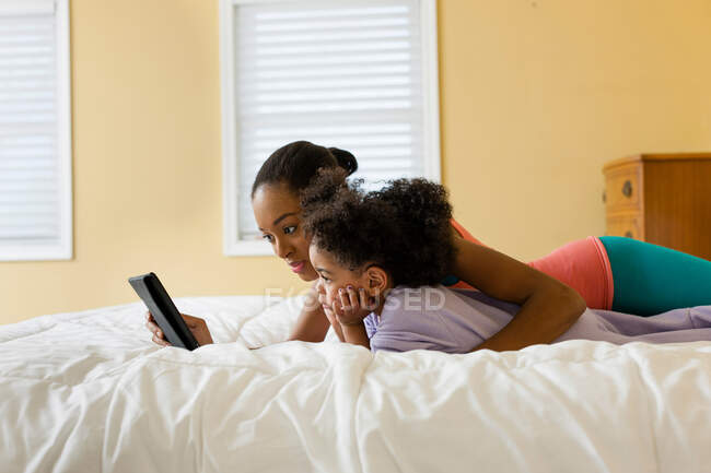 Mãe e filha deitadas na cama usando tablet digital — Fotografia de Stock