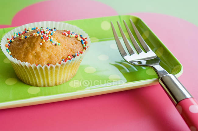 Cupcake decorato con spruzzi e forchetta sul piatto — Foto stock