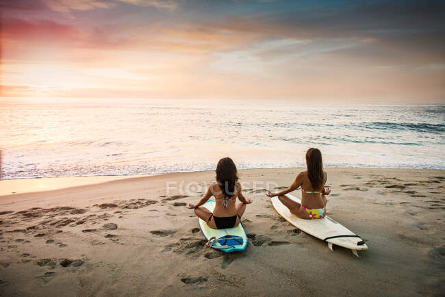 Dois surfistas, sentados em pranchas de surf na praia, meditando — Fotografia de Stock