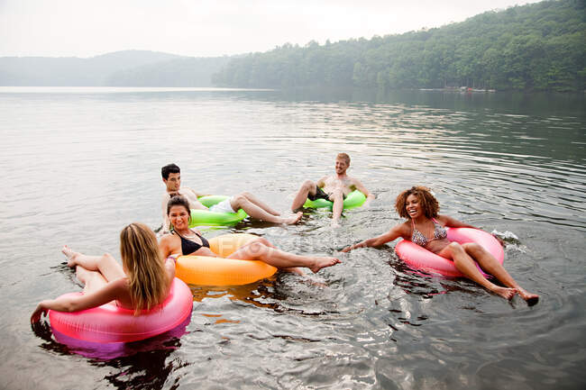 Friends playing in inflatable rings on lake — Stock Photo