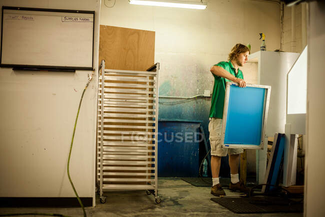 Homem segurando quadro na oficina de impressão de tela — Fotografia de Stock