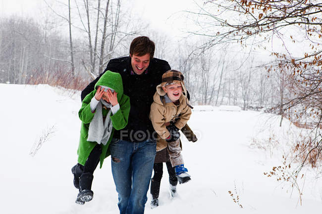 Отец несет сына и дочь в снегу — стоковое фото